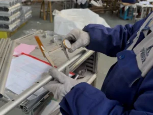 Un inspecteur mesure un profilé en aluminium extrudé à l'aide d'un pied à coulisse à côté d'une fiche de contrôle.