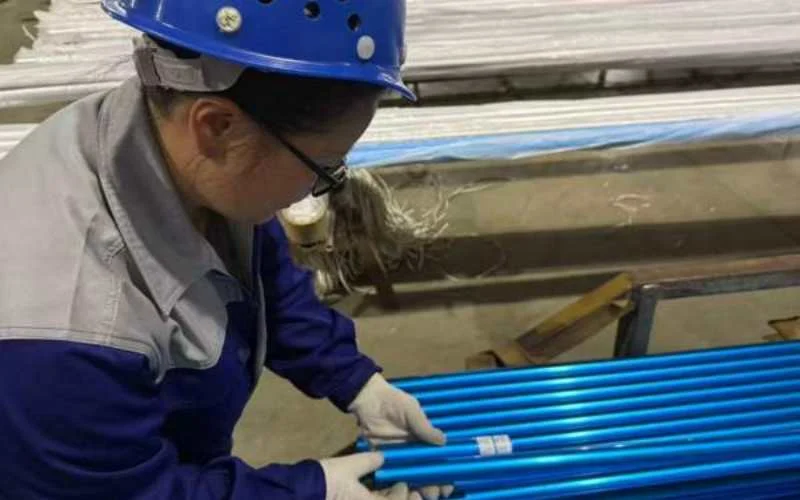 Inspector con casco revisando tubos de aluminio anodizado azul en un bastidor de producción.