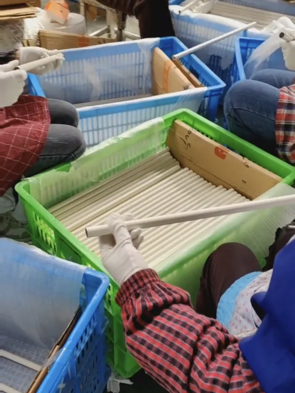 Workers inspecting and sorting finished grey push-button telescopic pole sections