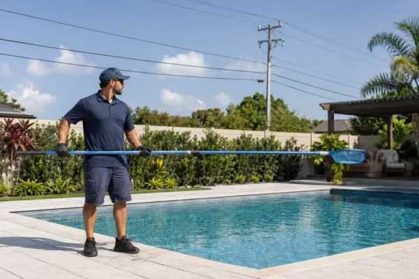 Pool technician carrying a long pool pole horizontally away from overhead power lines