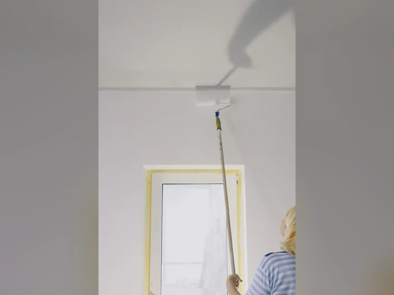 Roller on an extension pole painting the wall near a ceiling edge