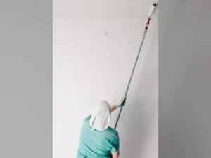 Un peintre guide un rouleau sur un plafond à l'aide d'une longue perche télescopique.